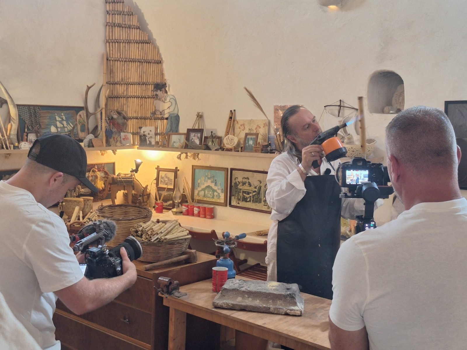 A craftsman heats a reed with a torch to shape a flute while the crew films, September 2026
